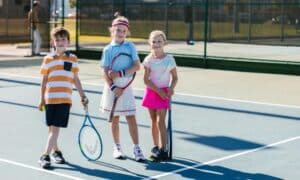 Junior group tennis lesson in Newcastle with three kids holding racquets