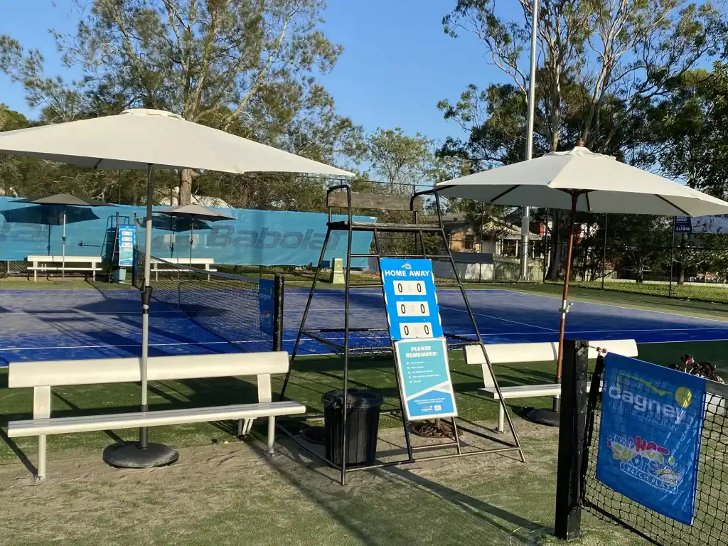 Tennis court facilities at Cagney Tennis Academy in Eleebana near Warners Bay, including seating, shade umbrellas and scoreboard